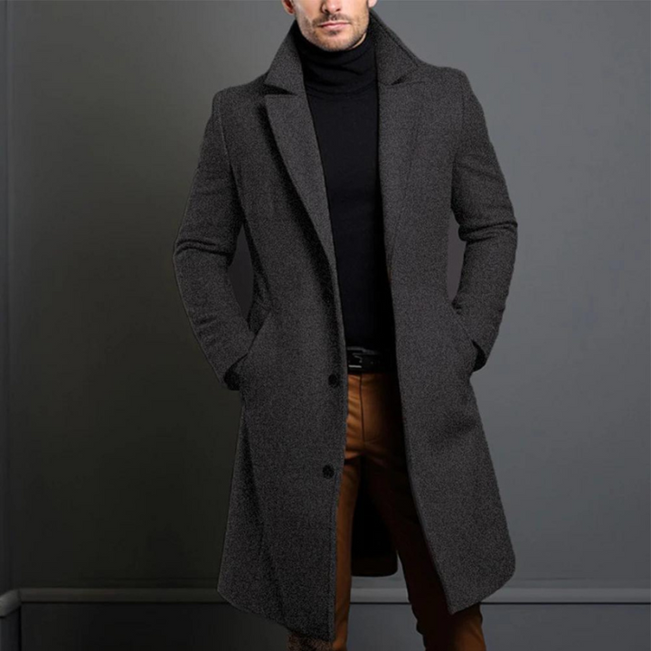 Manteau long en version gris anthracite chiné, porté par un homme en col roulé noir et pantalon marron. 3