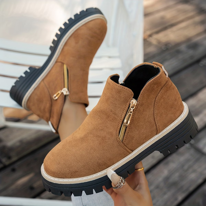 Bottines camel en daim à fermeture éclair dorée sur le côté, semelle crantée noire et liseré beige, portées en extérieur. 4