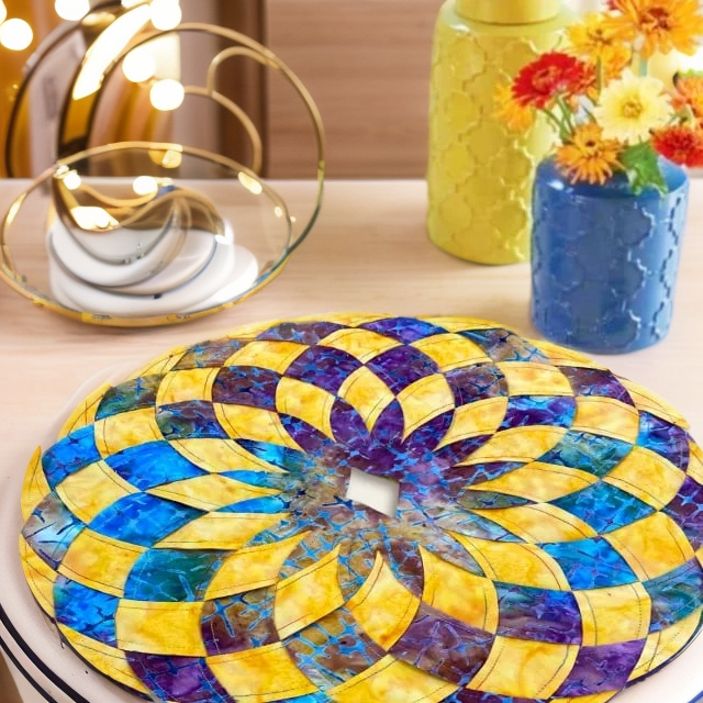 Gros plan sur un set de table en patchwork jaune, bleu et violet posé sur une table, avec des vases de fleurs colorés en arrière-plan. 9