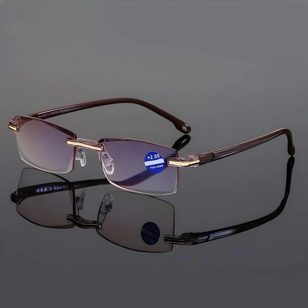 Lunettes sans monture à branches brunes et charnières dorées, posées sur une surface réfléchissante grise avec leur reflet. 7