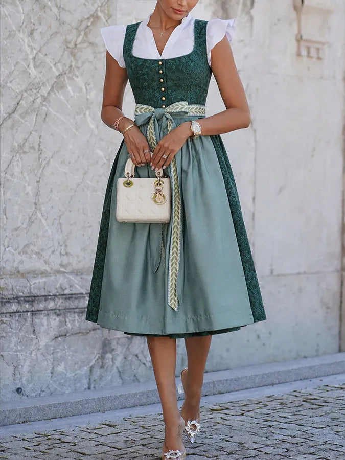 Femme en pied devant un mur de pierre claire, la robe longue jusqu'aux genoux, tablier bleu-vert et ruban noué à la taille. 4