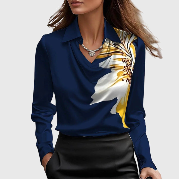 Blouse bleu marine à col drapé avec grande fleur blanche et jaune imprimée sur l'épaule, portée avec une jupe noire. 8