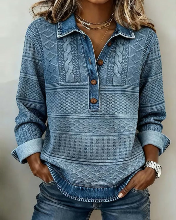 Sweat-shirt bleu à motifs torsadés et losanges, col chemise et boutons marron, porté par une femme les mains dans les poches. 1