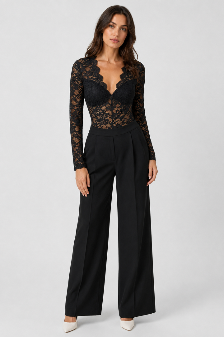 Femme en pied, de face, portant le body en dentelle noire avec un pantalon noir large à pinces et des escarpins blancs. 2