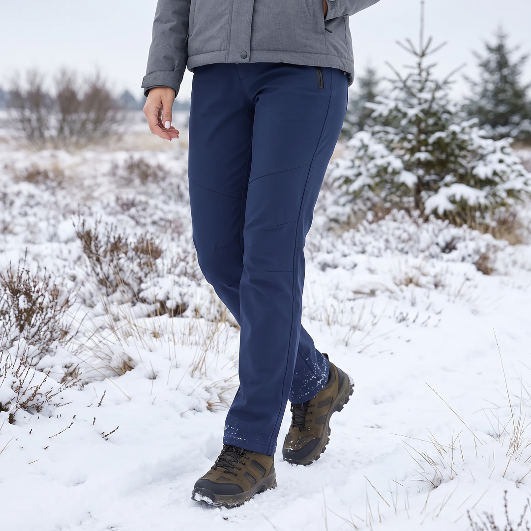 Femme en pantalon bleu marine et chaussures de randonnée marchant dans un paysage enneigé 1