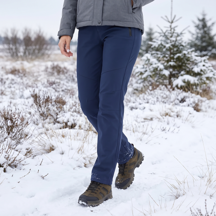 Femme en pantalon bleu marine et chaussures de randonnée marchant dans un paysage enneigé 1