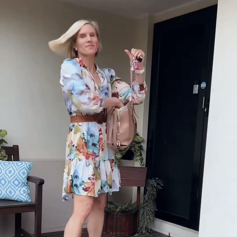 Femme blonde en robe fleurie, sac à l'épaule et clés à la main, secouant ses cheveux lisses devant une porte. 8