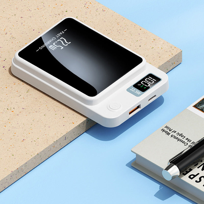 Chargeur blanc posé sur un support, montrant ses ports USB-A et USB-C, son bouton et son afficheur, près d'un livre et d'un stylo. 6