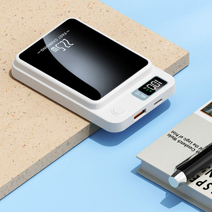 Chargeur blanc posé sur un support, montrant ses ports USB-A et USB-C, son bouton et son afficheur, près d'un livre et d'un stylo. 6