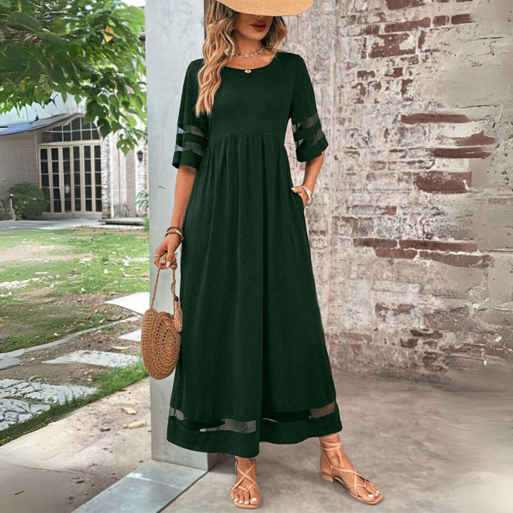 Robe longue vert foncé à manches évasées ajourées, portée avec chapeau de paille et sac rond en osier devant un mur de briques. 6