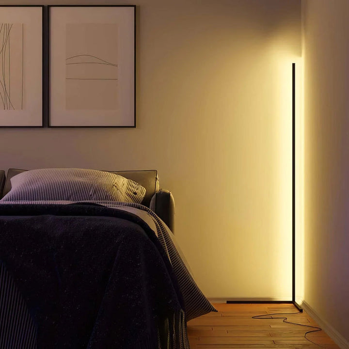 Lampadaire d'angle allumé en lumière chaude dans une chambre, câble au sol visible près du lit 4