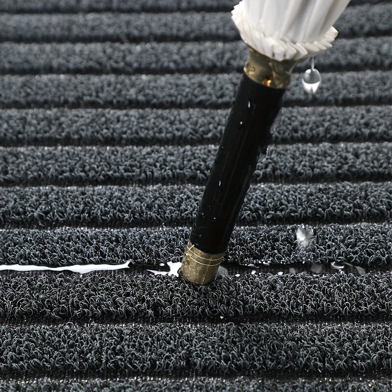 Gros plan sur les boucles épaisses du tapis gris, avec un parapluie fermé dont l'eau s'écoule dans les fibres. 3