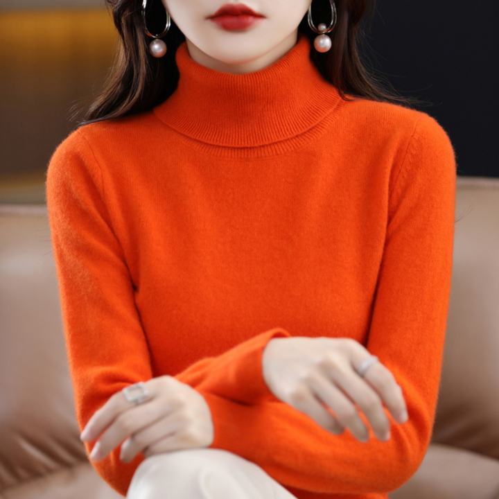 Pull orange à col roulé porté par une femme assise, mains posées sur les genoux, vue de face. 10