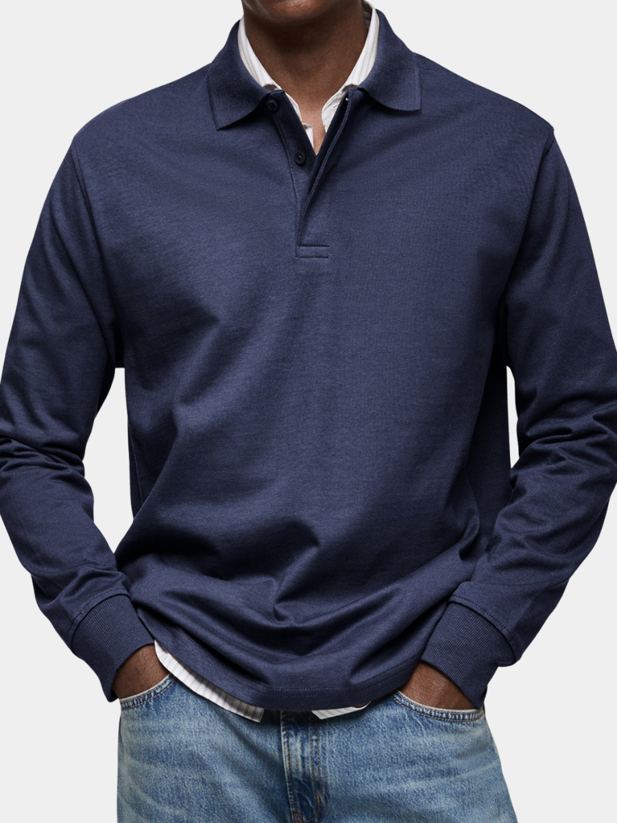 Polo bleu marine à manches longues porté par un homme, mains dans les poches, sur chemise rayée et jean, vue de face rapprochée. 1