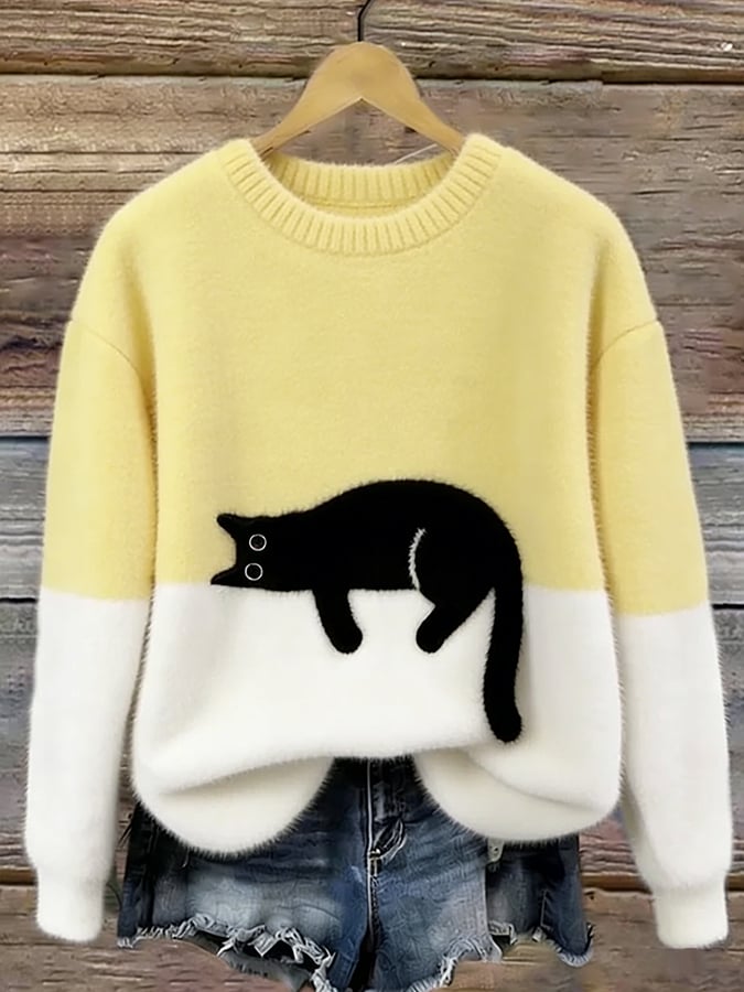 Pull duveteux jaune pâle et blanc avec chat noir allongé, accroché sur cintre devant des planches de bois 7