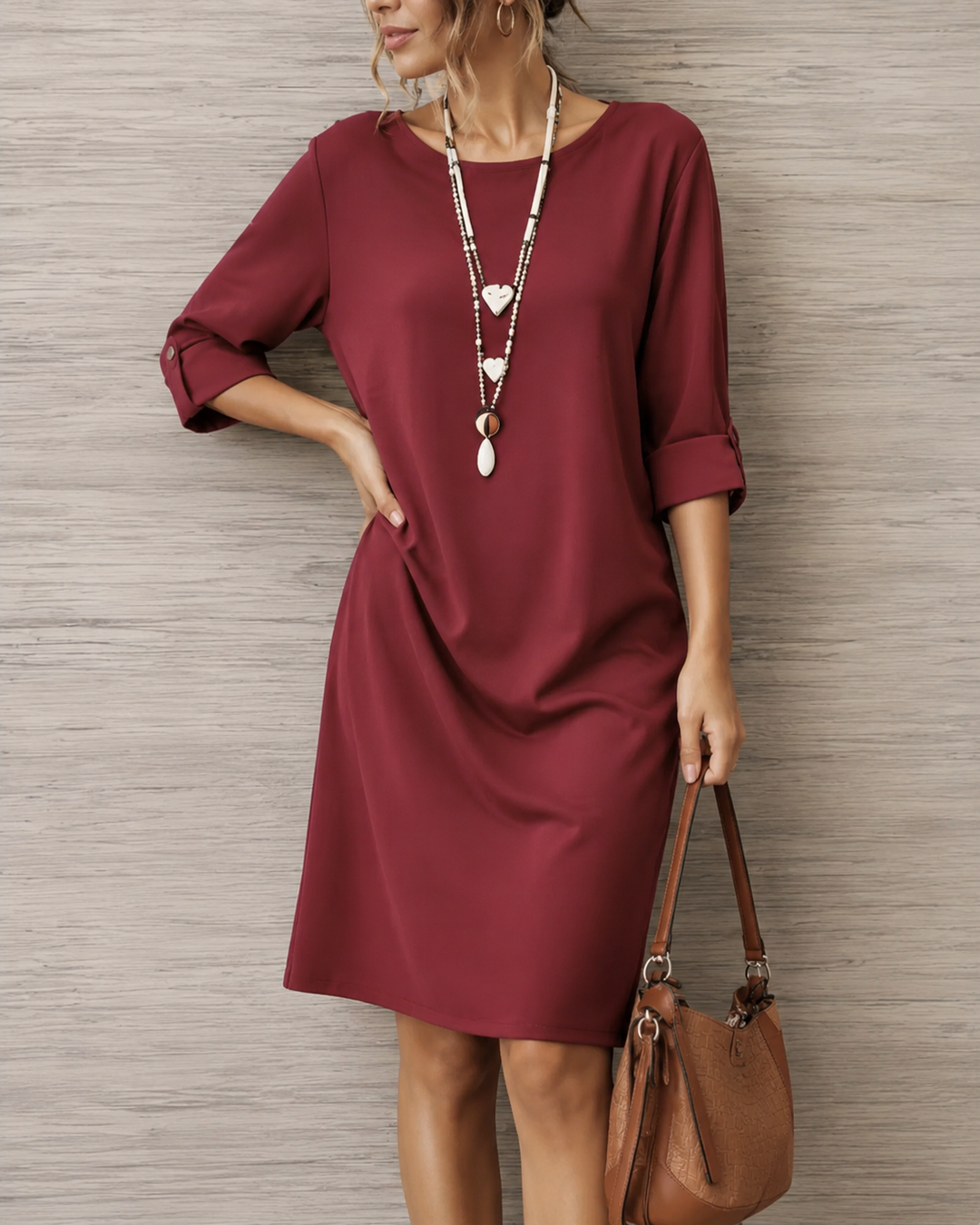Gros plan sur une robe bordeaux à manches retroussées, portée avec un long collier et un sac marron 6