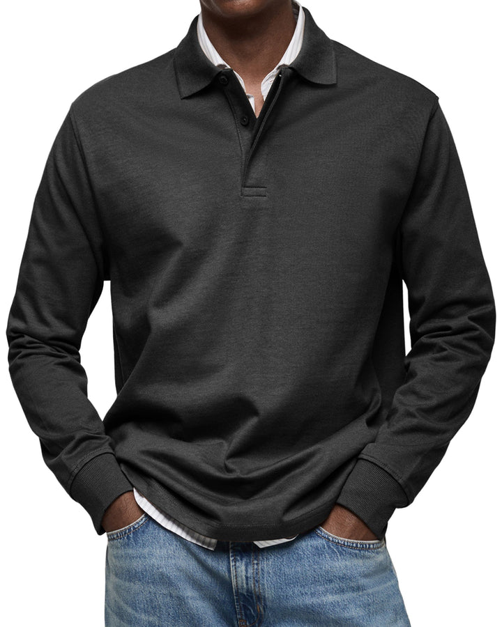 Polo à manches longues noir porté par un homme, mains dans les poches, col boutonné, chemise rayée apparente et jean bleu. 4