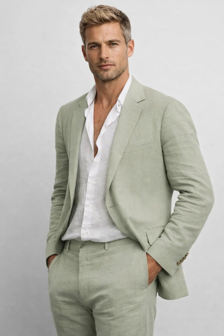 Mannequin en costume vert sauge sur chemise blanche ouverte, les mains dans les poches, vue en buste sur fond gris clair. 1