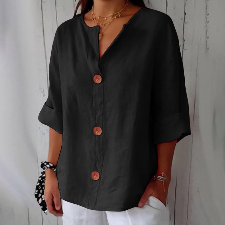 Même blouse en noir, portée avec un pantalon blanc, trois boutons en bois marron bien visibles sur la patte de boutonnage. 11