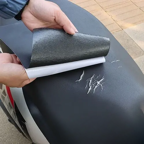 Mains décollant le film d'un patch noir au-dessus de fissures claires sur une selle de scooter 3