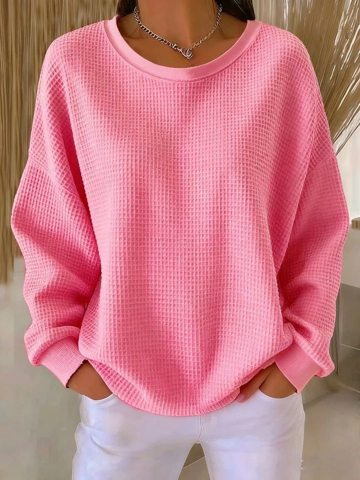 Pull gaufré rose clair à col rond et manches longues, porté mains dans les poches avec un pantalon blanc. 10
