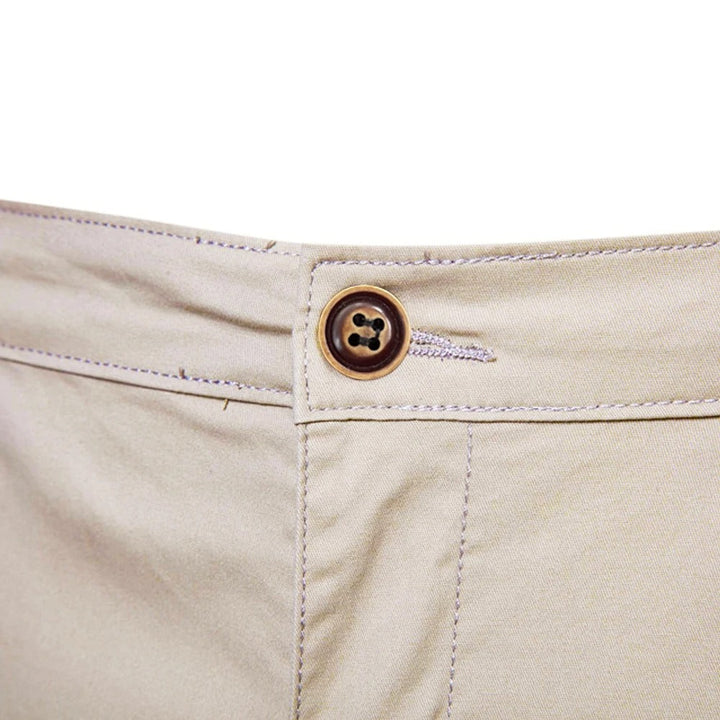 Gros plan sur le bouton marron à quatre trous et la boutonnière à la taille du short beige. 5