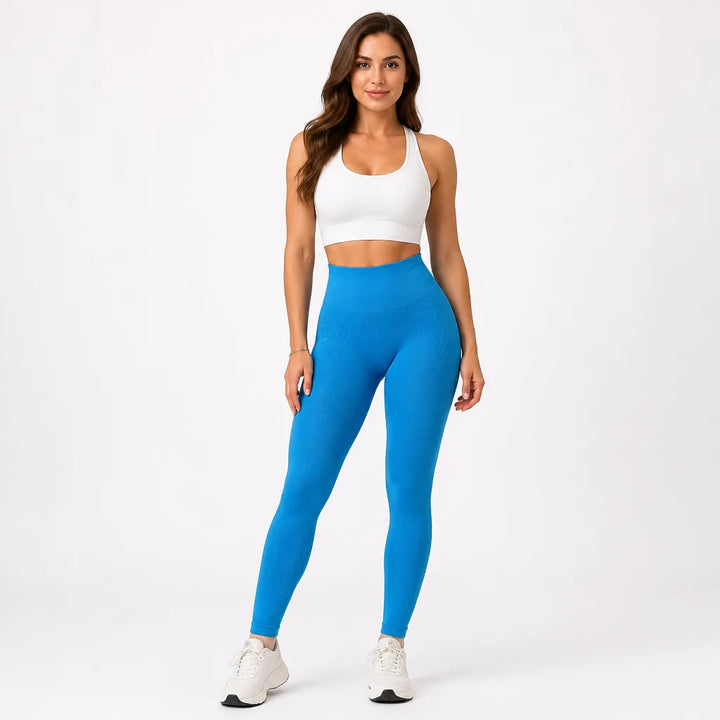 Femme de face en legging bleu vif taille haute, brassière blanche, bras le long du corps, baskets blanches. 12