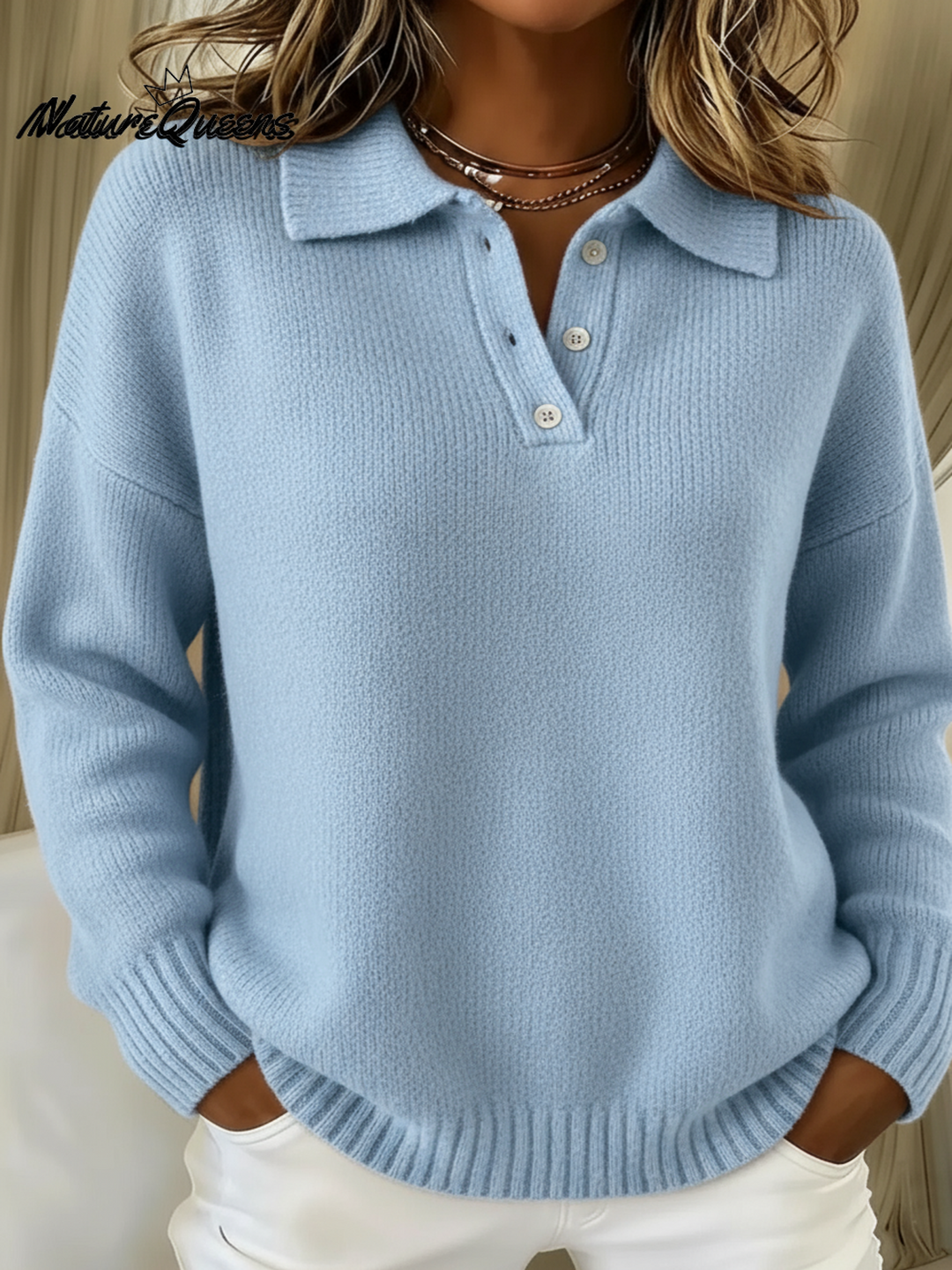 Femme portant le pull en tricot bleu clair, col polo boutonné, mains dans les poches d'un pantalon blanc, vue de face. 1