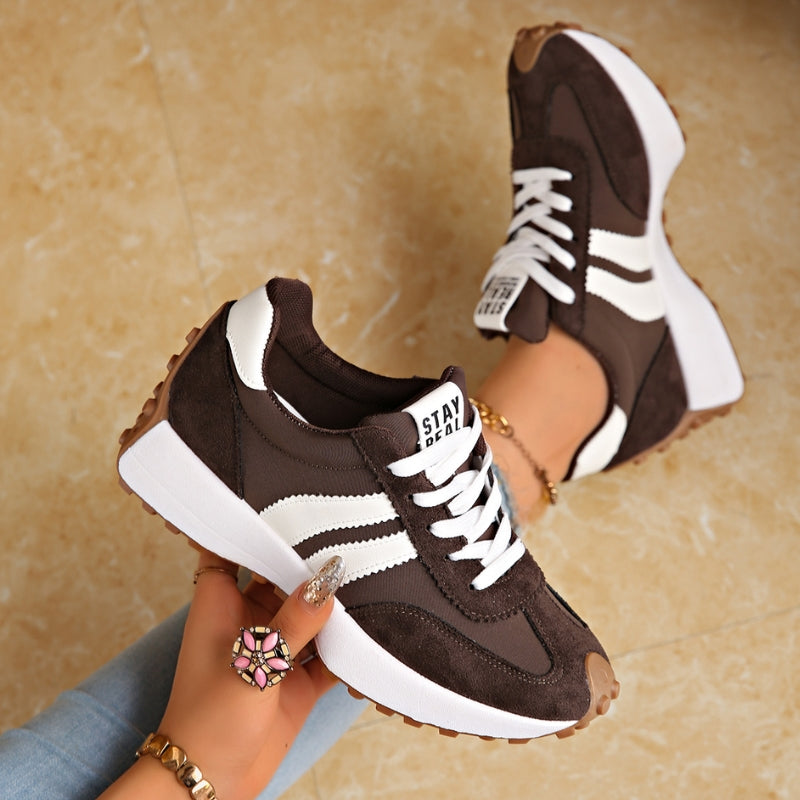 Baskets marron foncé à bandes blanches, tenues en main au-dessus d'un sol en marbre beige 3
