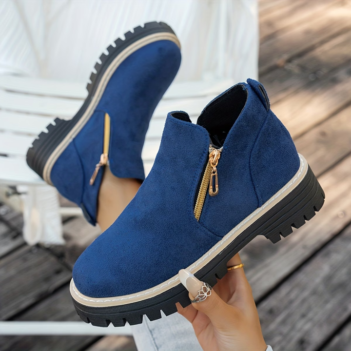 Bottines bleu marine en daim avec zip doré sur le côté et semelle crantée noire, portées pieds relevés sur un banc. 6