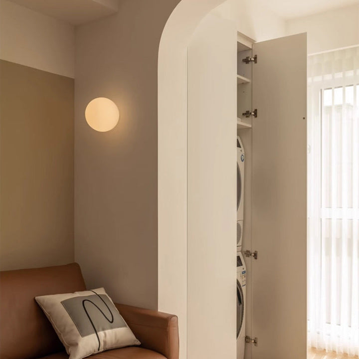Applique sphérique allumée sur un mur beige, près d'un canapé en cuir et d'une arche 4