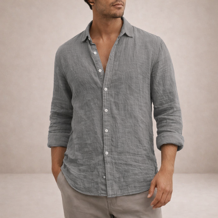 Chemise en lin grise portée par un homme, col ouvert, manches retroussées, une main dans la poche du pantalon beige. 2