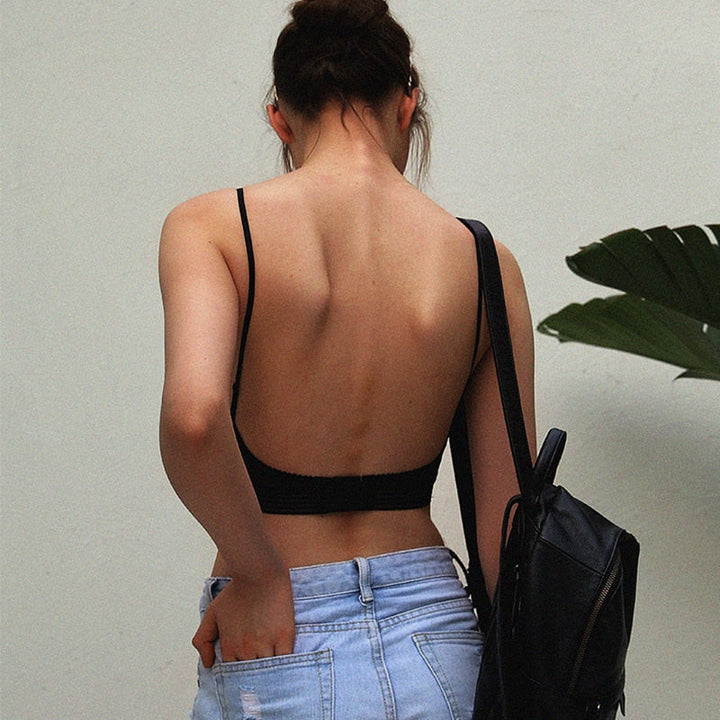 Vue de dos d'une femme en soutien-gorge noir au dos entièrement dégagé, avec bretelles fines, jean clair et sac à dos. 2