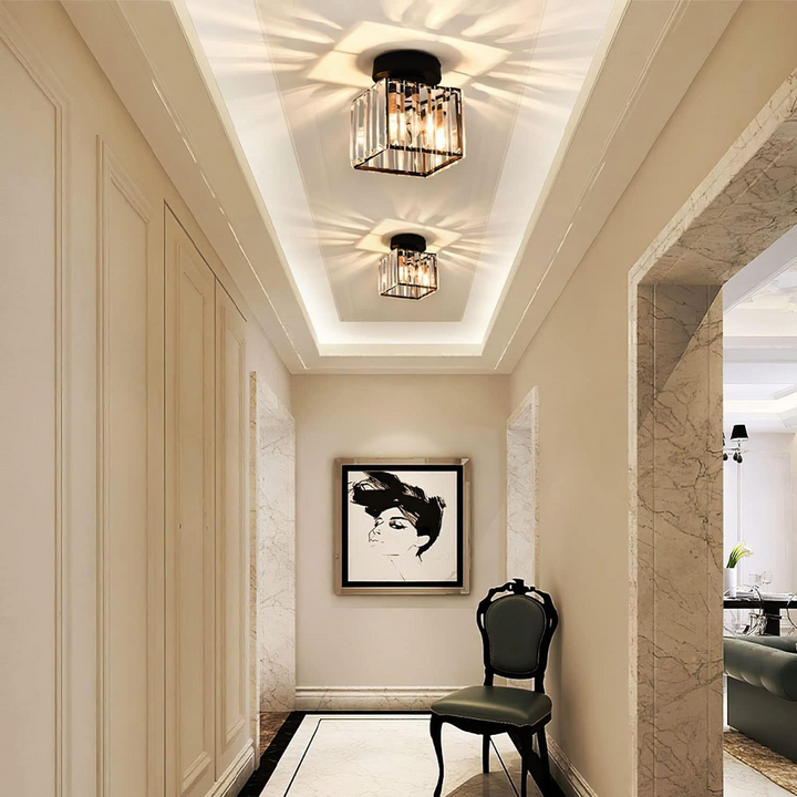 Deux plafonniers carrés en cristal éclairant un long couloir de style classique, avec un tableau et une chaise au fond. 4