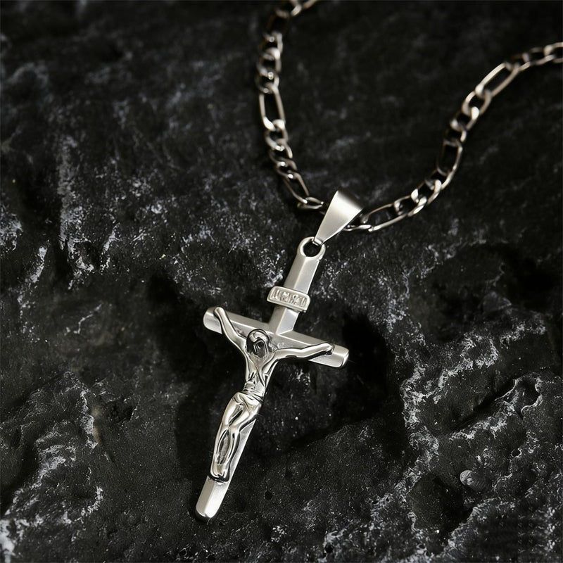 Crucifix argenté sur chaîne Figaro posé sur une roche sombre texturée 10