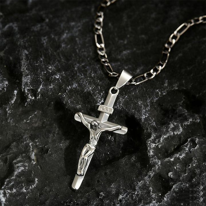 Crucifix argenté sur chaîne Figaro posé sur une roche sombre texturée 10