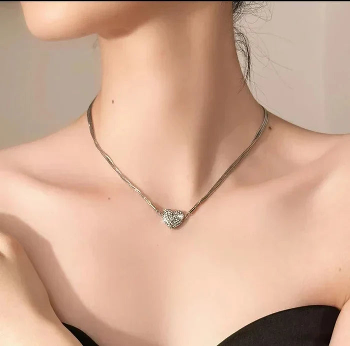 Collier argenté à cœur serti de strass porté par une femme aux épaules dénudées, vue rapprochée sur le décolleté. 3