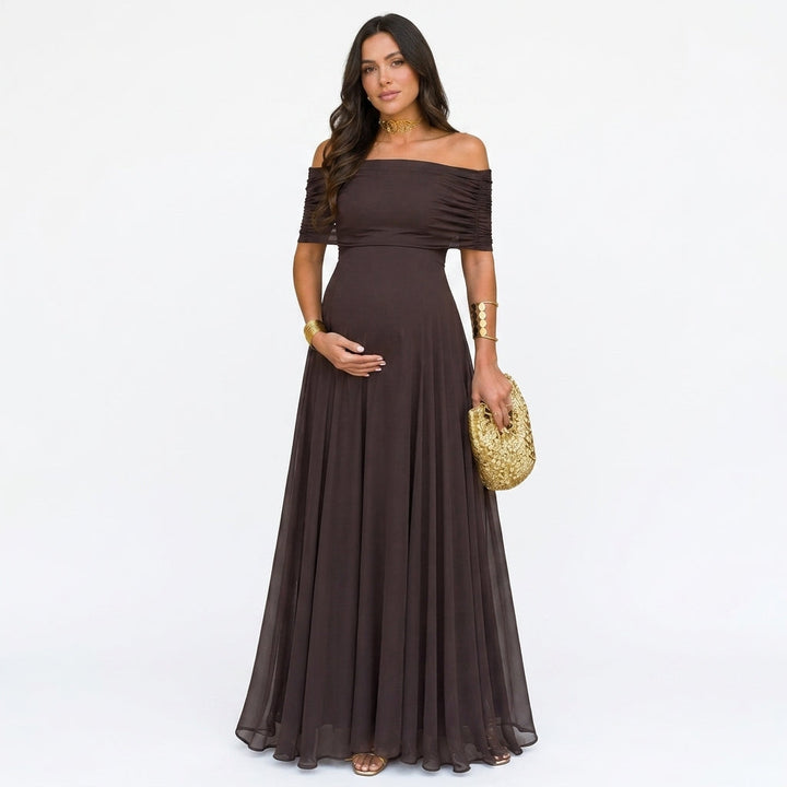 Femme enceinte de face en robe longue brune en voile, épaules dénudées, pochette dorée à la main 1