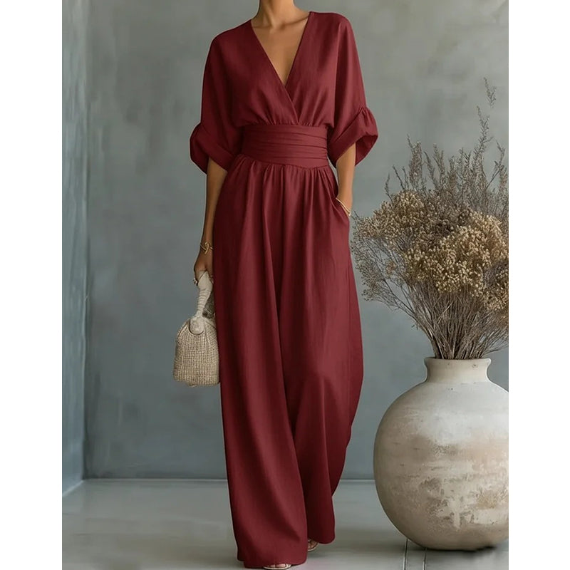 Combinaison bordeaux cadrée sans le visage, détail de la taille plissée et du pantalon large devant un grand vase. 8