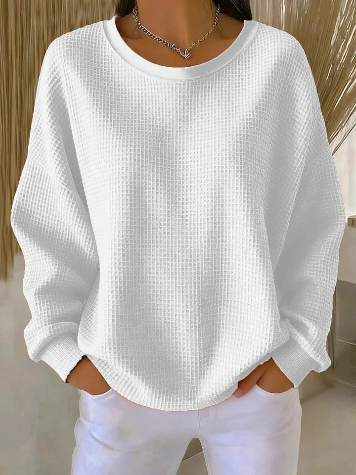 Pull gaufré blanc à col rond et poignets côtelés, porté avec un pantalon blanc devant un décor de paille. 6