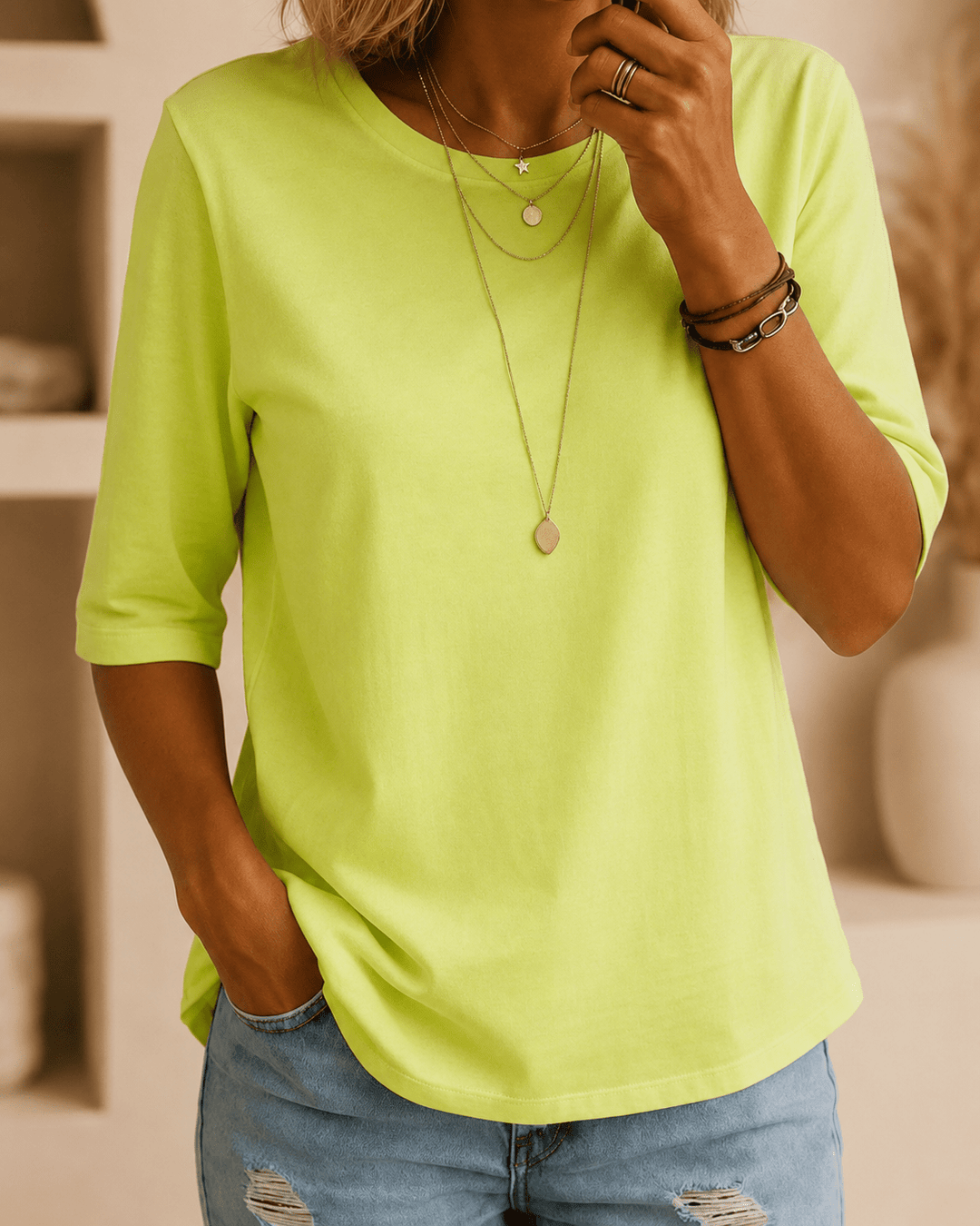 Femme portant le tee vert néon à col rond, main dans la poche d'un jean délavé, avec colliers fins superposés et bracelets. 1