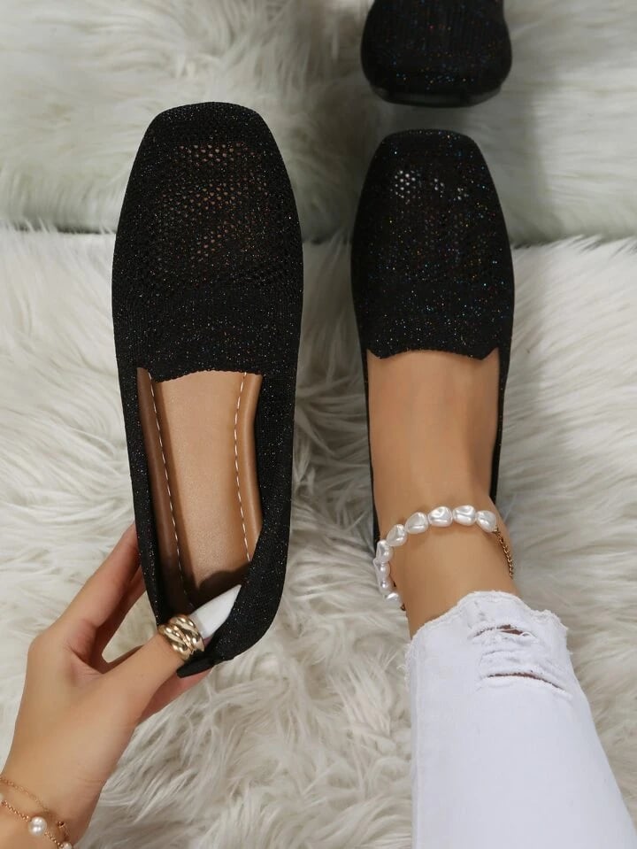 Vue de dessus de ballerines noires pailletées en mesh ajouré, l'une tenue à la main pour montrer la semelle intérieure souple. 1