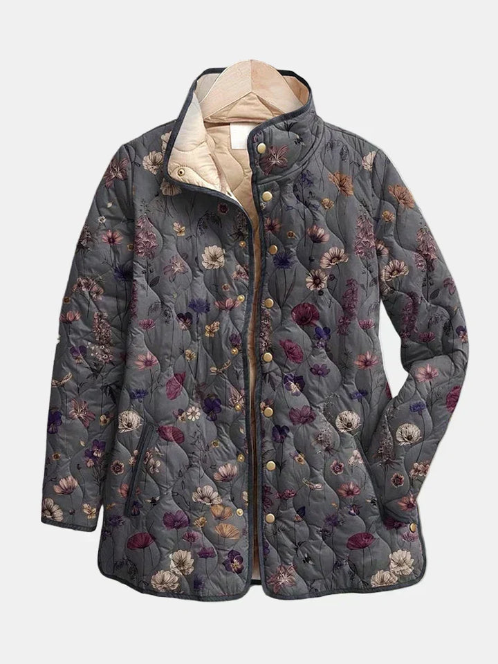Veste matelassée grise à motif floral présentée sur cintre, fermée par des boutons-pression dorés, avec col montant et doublure beige. 2