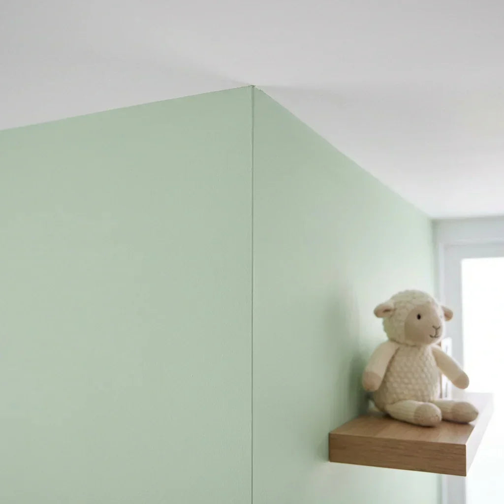 Angle d'un mur peint en vert clair, avec une peluche d'agneau posée sur une étagère en bois 5
