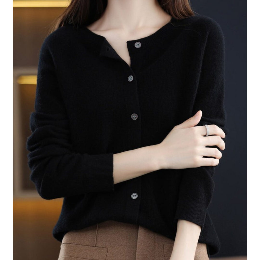 Cardigan noir à col rond et boutons gris, porté avec un pantalon camel, bras croisé devant le buste. 6