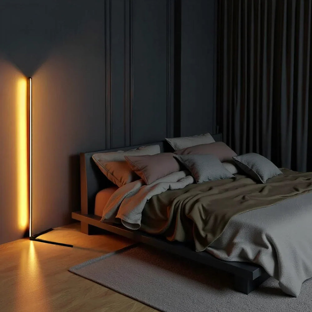 Lampadaire allumé en lumière ambrée dans une chambre sombre, à côté d'un lit bas aux coussins 2