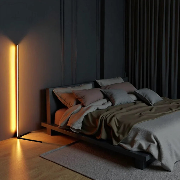 Lampadaire allumé en lumière ambrée dans une chambre sombre, à côté d'un lit bas aux coussins 2