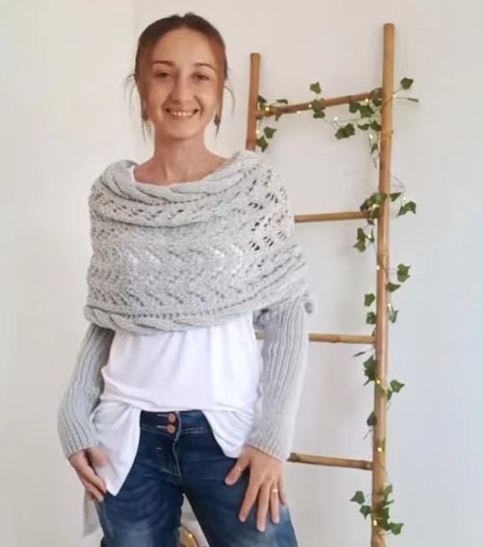 Châle gris clair avec col drapé en torsades et manches intégrées, porté de face par la modèle souriante, mains aux hanches. 15
