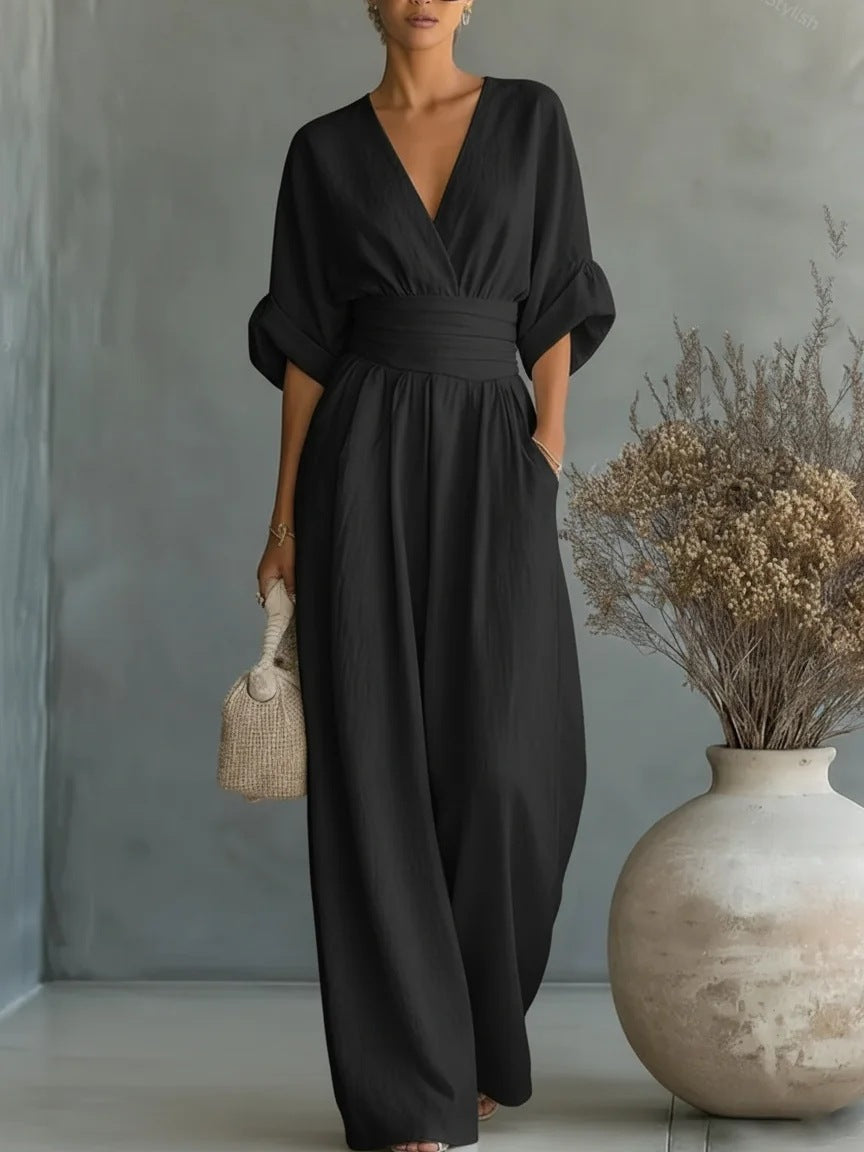 Combinaison noire portée de face, décolleté en V, manches mi-longues retroussées et jambes larges, avec un sac en paille. 5