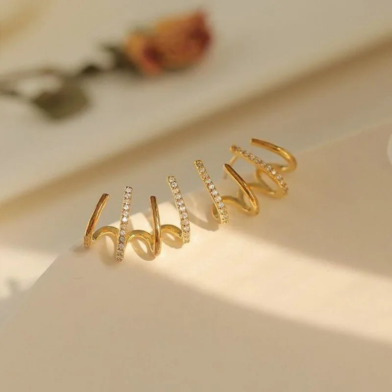 Paire de boucles dorées à griffes scintillantes sur fond clair, une fleur séchée floue à l'arrière-plan 8